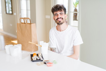 Young man eating asian sushi from home delivery happy face smiling with crossed arms looking at the camera. Positive person.