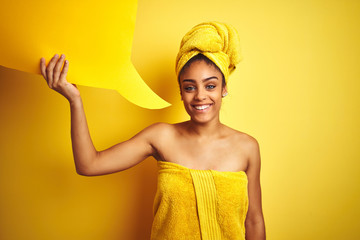 Afro woman wearing towel after shower holding speech bubble over isolated yellow background with a happy face standing and smiling with a confident smile showing teeth