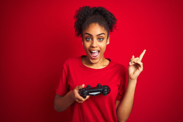African american gamer woman playing video game using joystick over isolated red background very happy pointing with hand and finger to the side © Krakenimages.com