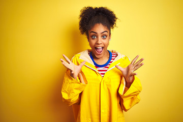 Young african american woman wearing rain coat over isolated yellow background celebrating crazy and amazed for success with arms raised and open eyes screaming excited. Winner concept