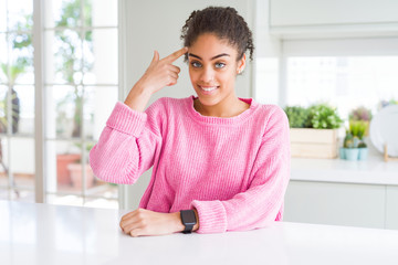 Beautiful african american woman with afro hair wearing casual pink sweater Smiling pointing to head with one finger, great idea or thought, good memory