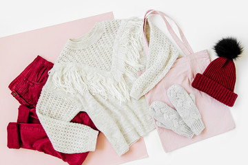 Gray warm knitted sweater, mittens with vinous winter hat and trouserson on white background. Women's stylish autumn or winter clothes. Flat lay, top view.