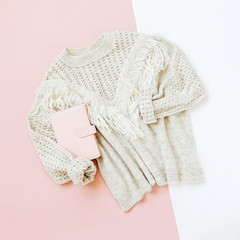 Obraz na płótnie Canvas Gray warm knitted sweater with book on pale pink background. Women's stylish winter clothes. Flat lay, top view.