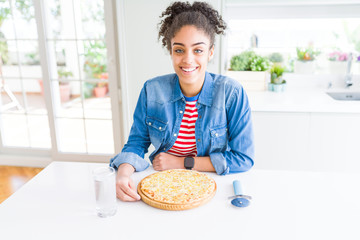 Young african american woman eating homemade cheese pizza with a happy face standing and smiling with a confident smile showing teeth