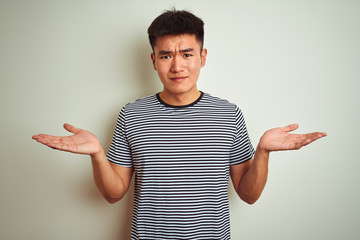 Young asian chinese man wearing striped t-shirt standing over isolated white background clueless...