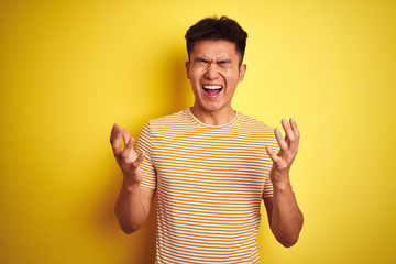 Young asian chinese man wearing t-shirt standing over isolated yellow background celebrating mad...