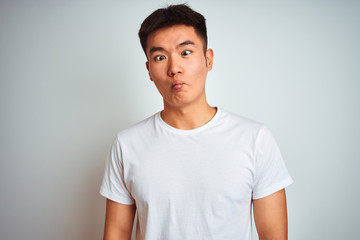 Fototapeta premium Young asian chinese man wearing t-shirt standing over isolated white background making fish face with lips, crazy and comical gesture. Funny expression.