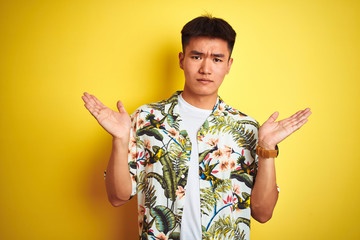 Asian chinese man on holiday wearing summer shirt over isolated yellow background clueless and...