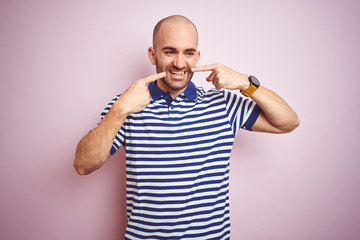 Fototapeta premium Young bald man with beard wearing casual striped blue t-shirt over pink isolated background smiling cheerful showing and pointing with fingers teeth and mouth. Dental health concept.