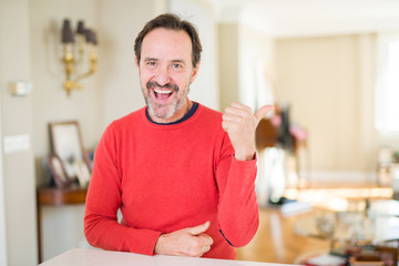 Handsome middle age man at home smiling with happy face looking and pointing to the side with thumb up.
