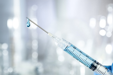 Syringe filled with blue drug and dripping from the needle. Vaccine or medicine concept.