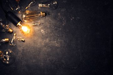Vintage old light bulb glowing yellow on rough dark background surrounded by burnt out bulbs. Idea,...