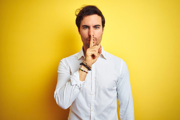 Young handsome businessman wearing elegant shirt standing over isolated yellow background asking to be quiet with finger on lips. Silence and secret concept.