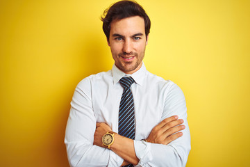 Young handsome businessman wearing elegant shirt and tie over isolated yellow background happy face smiling with crossed arms looking at the camera. Positive person.