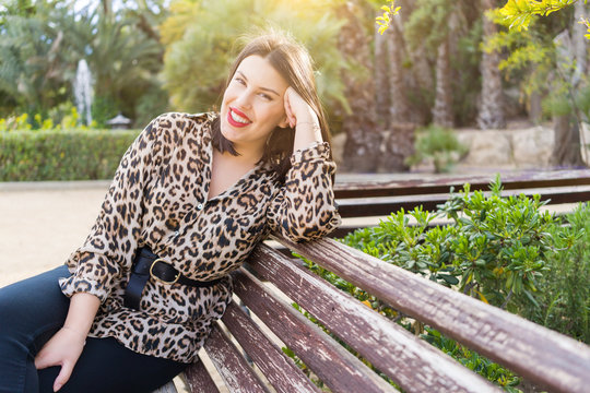 Young beautiful woman with red lips smiling happy sitting on a bench at garden