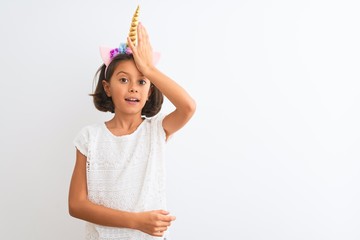 Beautiful child girl wearing unicorn diadem standing over isolated white background surprised with...