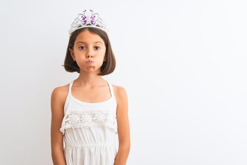 Beautiful child girl wearing princess crown standing over isolated white background puffing cheeks with funny face. Mouth inflated with air, crazy expression. © Krakenimages.com