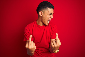 Young brazilian man wearing t-shirt standing over isolated red background Showing middle finger...