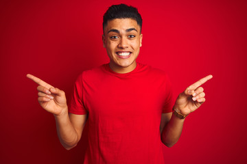 Young brazilian man wearing t-shirt standing over isolated red background smiling confident pointing with fingers to different directions. Copy space for advertisement