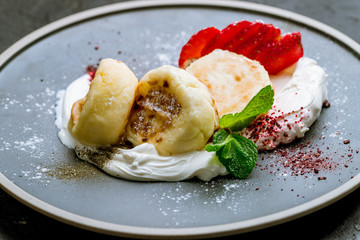 cheesecakes from cottage cheese with strawberry and cream on grey plate on black concrete table