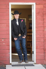 Young handsome cowboy groom posing in red barn door