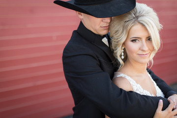 Romantic wedding portrait of cowboy groom and elegant bride in front of red barn
