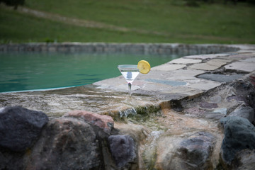 Glass of martini cocktail at swimming pool with ocean and palm tree background. A glass of blue martini cocktail welcome drink bar.Selective focus. season and holidays concept.