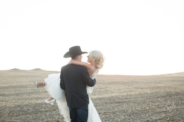 Cowboy groom carrying young bride in field