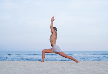 Fototapeta na wymiar Young woman practicing yoga on the beach. Virabhadrasana I pose