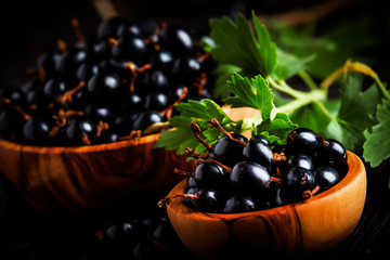 Fresh black currants in wooden bowls, on black kitchen table background, copy space, selective focus