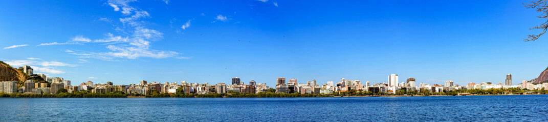 Panoramic image of the Ipanema and Leblon neighborhood and its buildings seen from the lagoon Rodrigo de Freitas with blue sky and calm waters