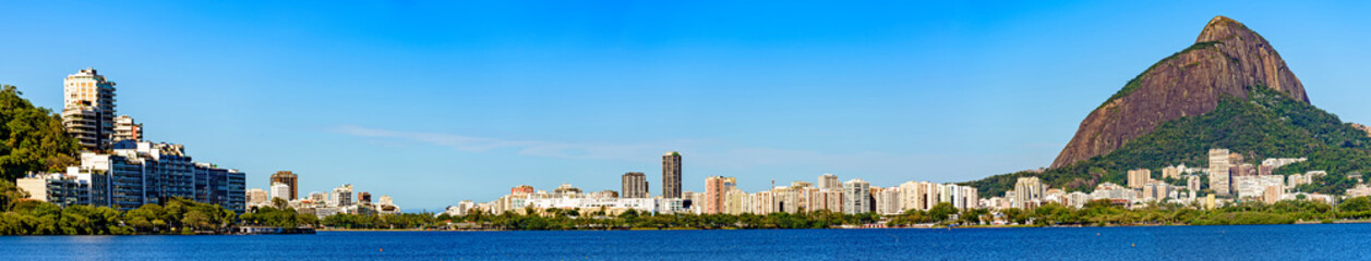 Fototapeta na wymiar Panoramic image of the Ipanema and Leblon neighborhood and its buildings seen from the lagoon Rodrigo de Freitas with blue sky and calm waters