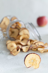 Fototapeta na wymiar Dried apples chips in glass jar on light background, vertical composition - Image