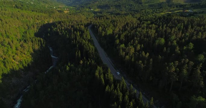 Aerial: Drone moving over motor home on country road amidst green trees by river - Borgund, Norway