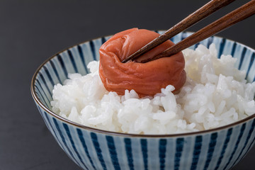 黒背景に白いご飯と梅干しを箸で割っているシーン寄り