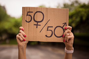 Gender equality concept as woman hands holding a paper sheet with male and female symbol over a crowded city street background. Woman protesting outdoor. Sex sign as a metaphor of social issue.