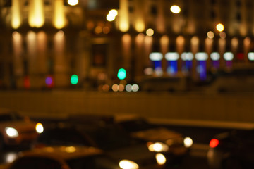 Fototapeta na wymiar Defocused night city life: cars, people and street lamps. Bokeh urban city background effect. Holidays, sale and retail concept. Design background