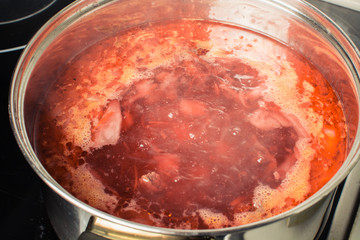 Red soup borscht cooked in large pan on stove.