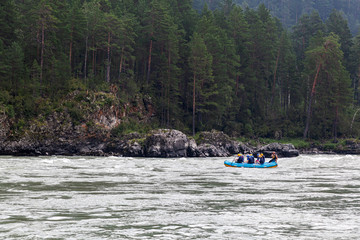 Fototapeta na wymiar A team of athletes in a blue inflatable boat rafts down a mountain river amid a green forest and mountains.rafting on a mountain river