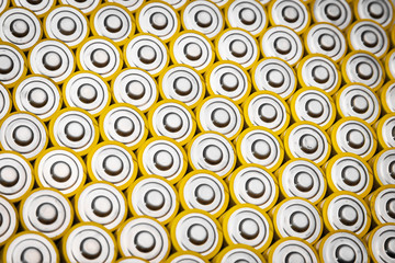 .Close view of batteries alkaline 1.5 Volts in size AA Several batteries in rows.A close-up of the same yellow batteries, lined up in even rows by positive charges. An unsafe way to use energy.