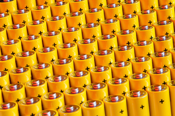 Alkaline battery aa size. Several batteries in rows.A close-up of the same yellow batteries, lined up in even rows by positive charges. An unsafe way to use energy.