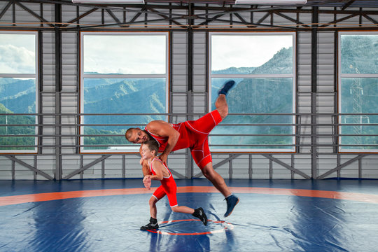 The little boy in sport tights wrestler throws over the hip adult male wrestler on a wrestling carpet in the gym. The concept of child power and martial arts training. 