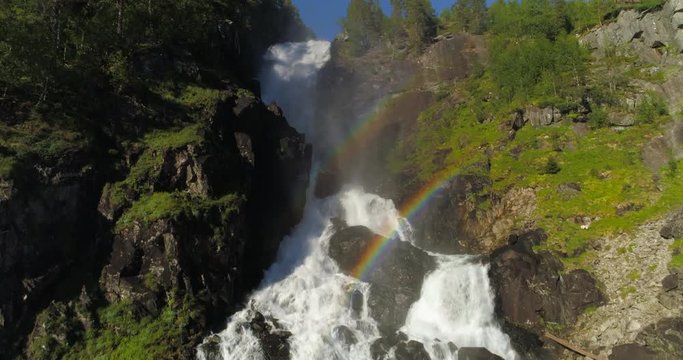 Aerial: Drone ascending over waterfall flowing through rocks with rainbow appearance - Borgund, Norway