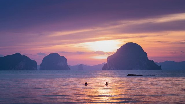 2 men swiming on the sea while sunset behind hte mountain, 4k timeslapse