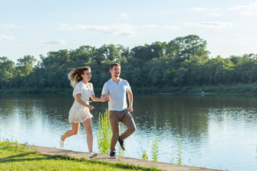 Fototapeta na wymiar Love and relationship concept - The happy man and woman running in a park near a lake