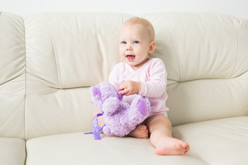 childhood, babyhood and people concept - happy little baby girl sitting on couch at home