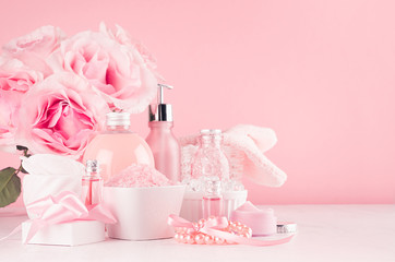 Cosmetics products for bath, spa - essential oil, bath salt, cream, liquid soap, towel and pink roses in delicate pastel pink  bathroom interior.