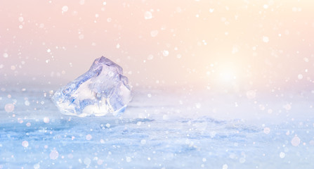 Ice on the frozen lake during snowfall at sunset. Beautiful winter nature background
