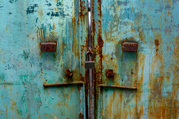The texture of the old metal gate painted in blue-green color with large stains of rust and a lock