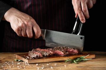 Slicing juicy beef steak by knife in chef hands closeup. Food cooking concept. Dark black background copy space. - 287129369